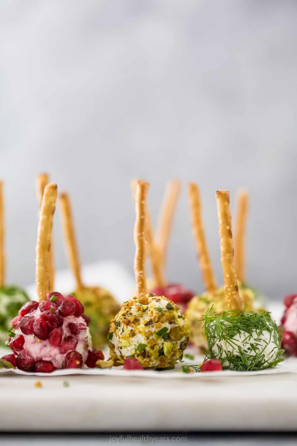 Homemade cheeseballs with pretzel "toothpicks" lined up on a cutting board