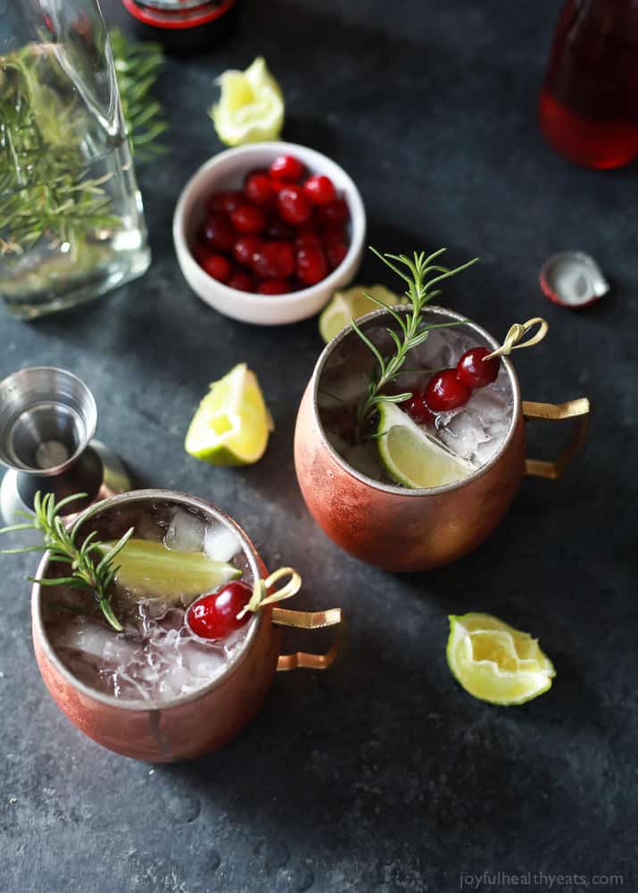 This festive cranberry Moscow mule recipe is made with rosemary-infused vodka that you can make at home! It's tart, refreshing, and light. Top view of two cranberry Moscow mule mugs with lime wedges and rosemary sprigs.