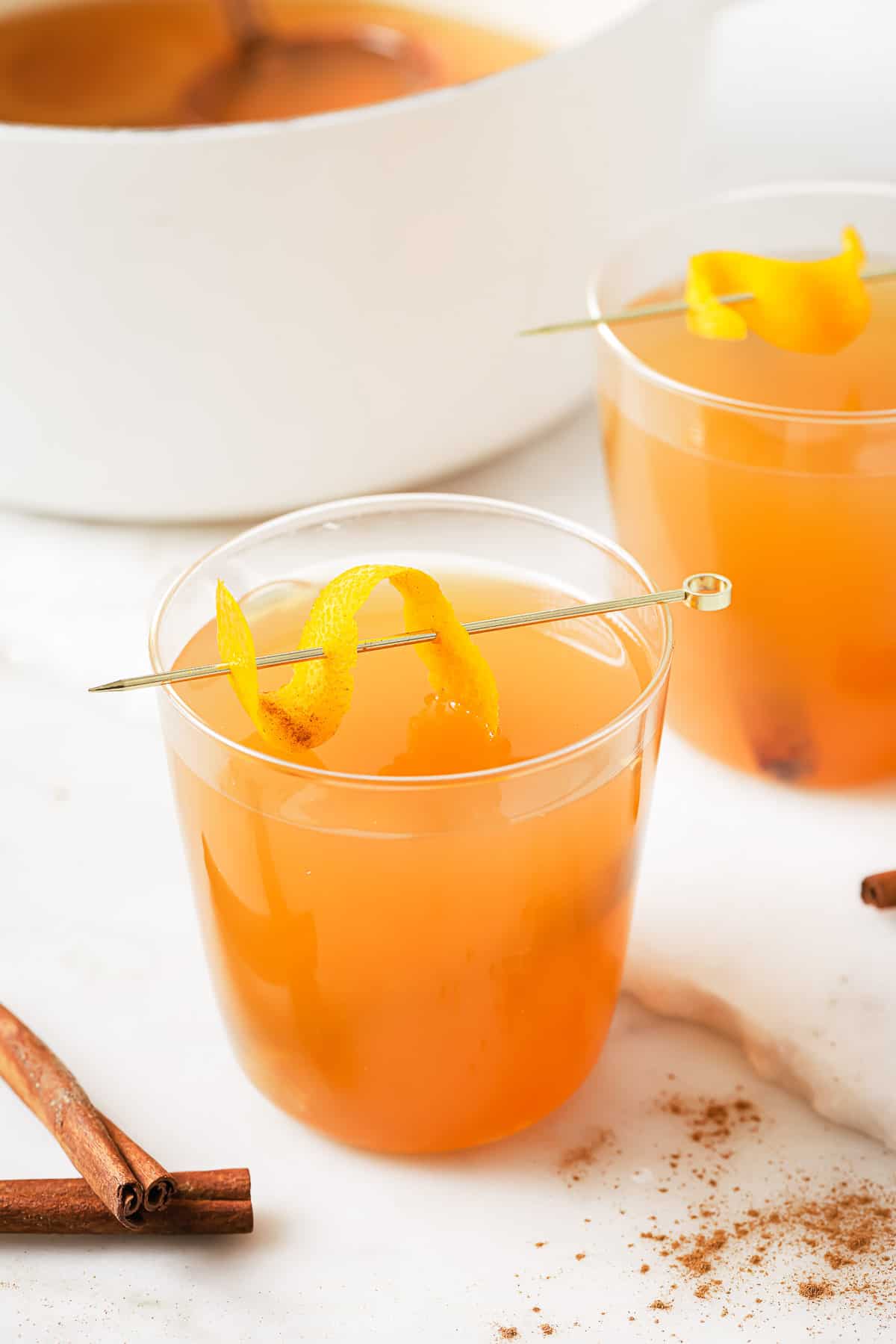 This tart crockpot hot apple cider is an effortless, slow-cooker version of your favorite warmly spiced fall drink. A glass of crockpot hot apple cider with an orange twist on a stirrer.