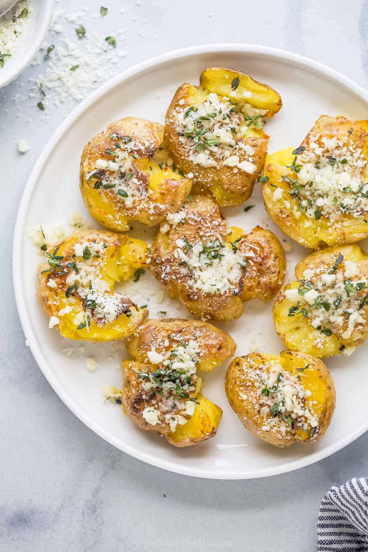 This crispy smashed potatoes recipe with hints of garlic, thyme, and fresh parmesan on top are a fancy but easy side everyone will love. Smashed potatoes with a garlic-herb mixture on top.
