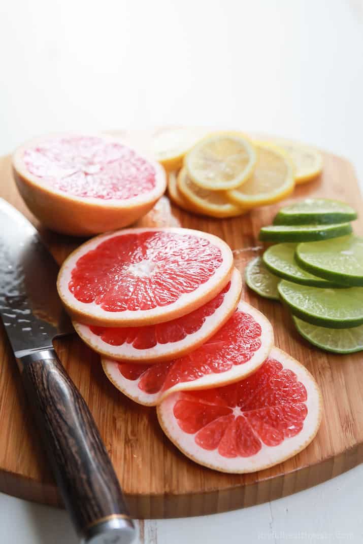 Slices of grapefruit, limes, and lemons on a wood cutting board. 