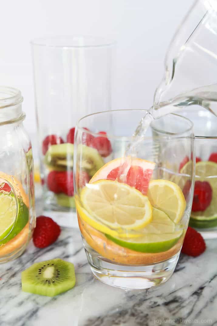 Pouring water into a glass filled with fresh fruit.