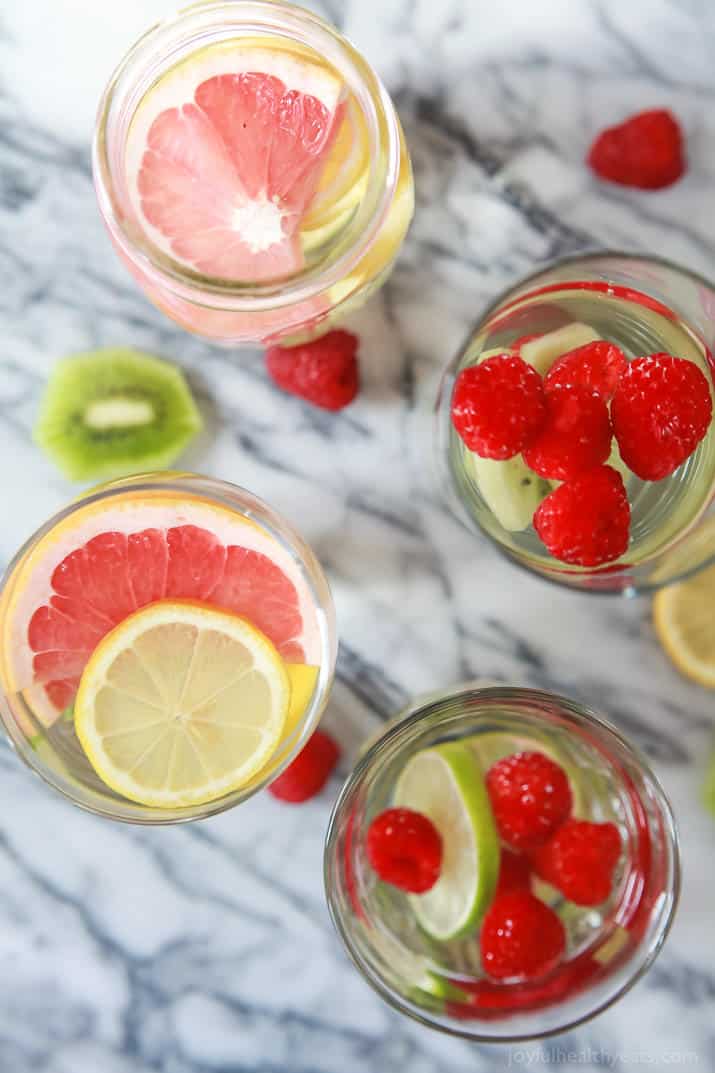 Overhead photo of glasses of fruit infused water with raspberries, lemon, limes, kiwi, and grapefruit. 