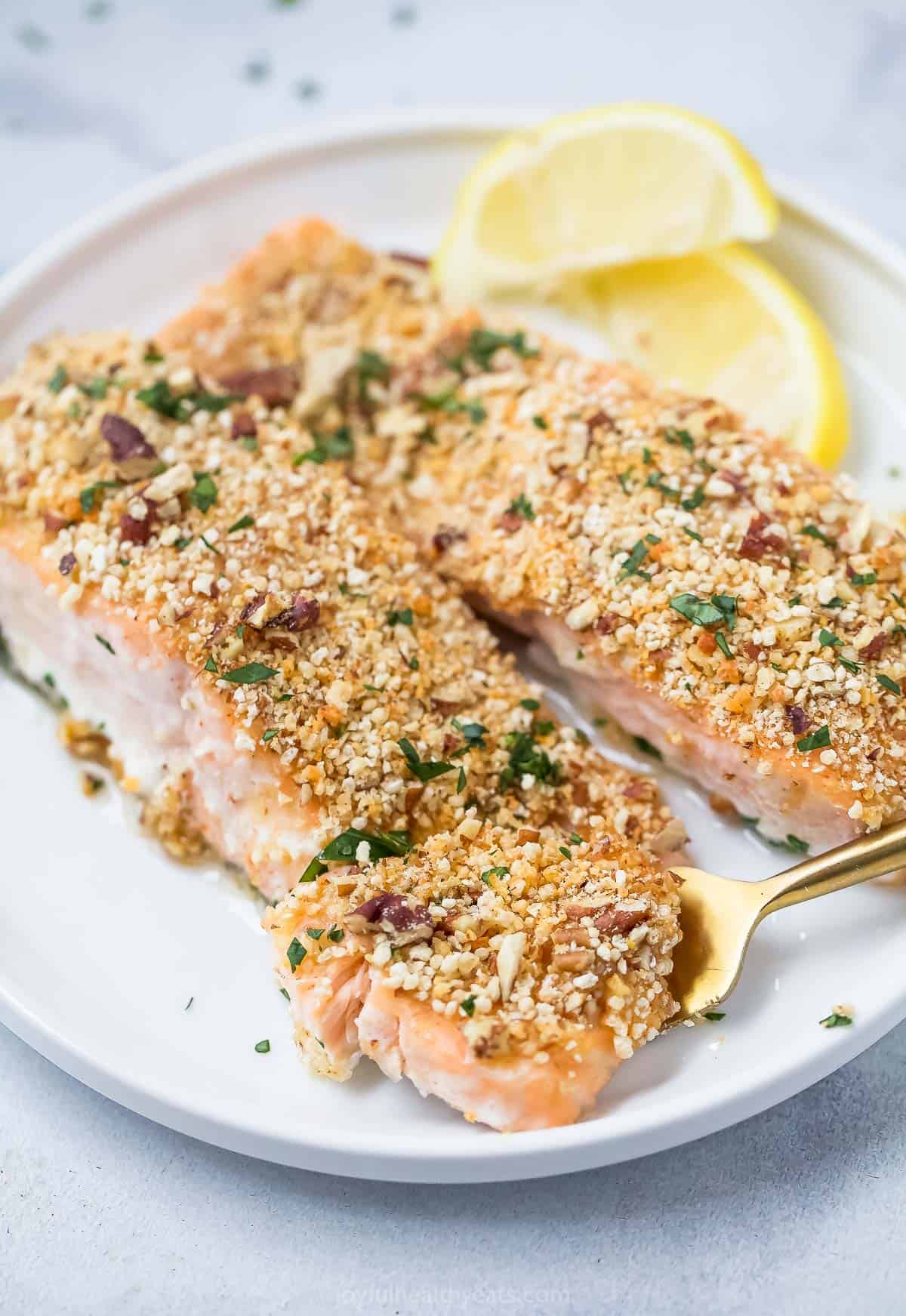 This flaky pecan crusted salmon recipe has a crispy exterior and a tender, buttery interior with hints of honey-mustard you'll love. Pecan crusted salmon with lemon wedges on the side.