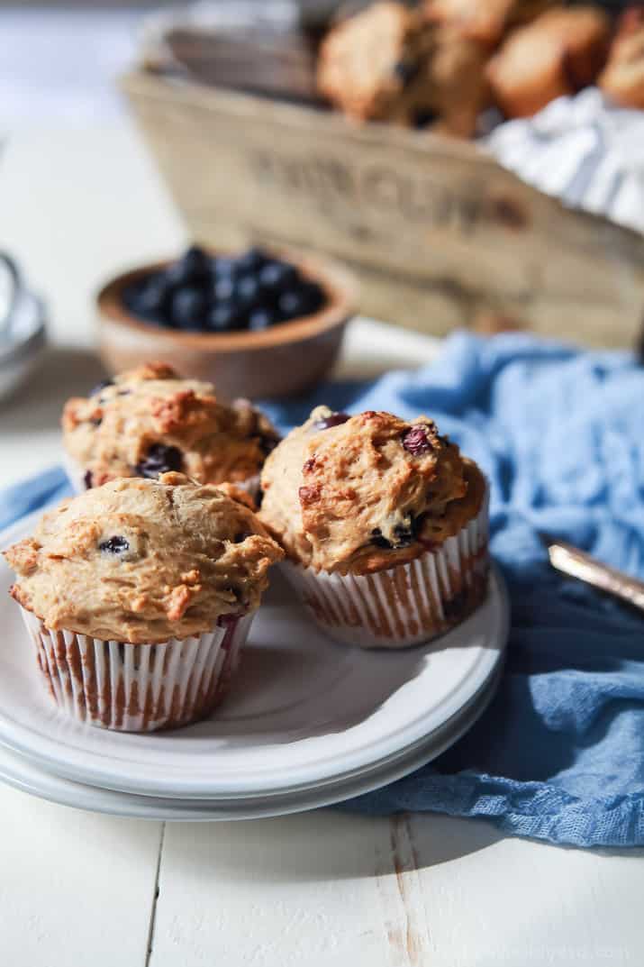 This spiced blueberry lemon muffins recipe with honey and applesauce are an easy way to have dessert for breakfast. Three blueberry lemon muffins on a serving plate.