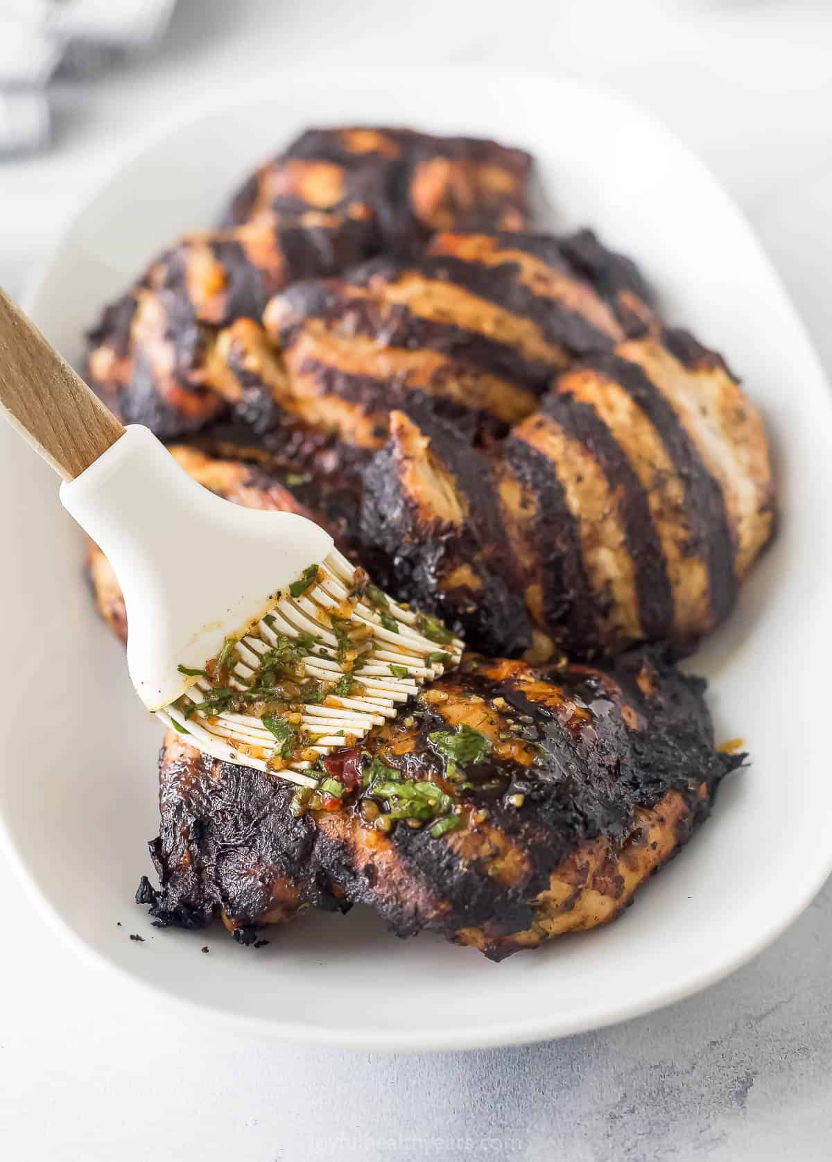 Brushing more marinade over the grilled chicken.