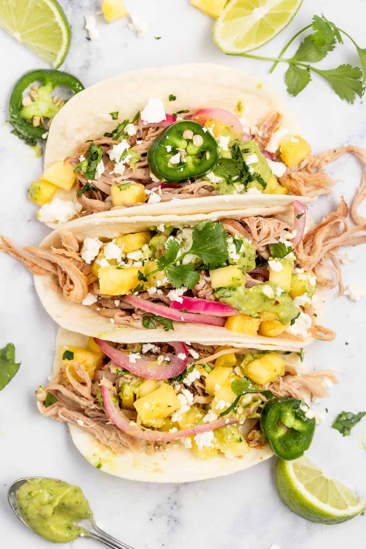 Loaded with crunchy toppings, these crockpot pork carnitas tacos will be your new taco-night favorite. They're juicy, easy, and effortless! Three pork carnitas tacos with toppings.