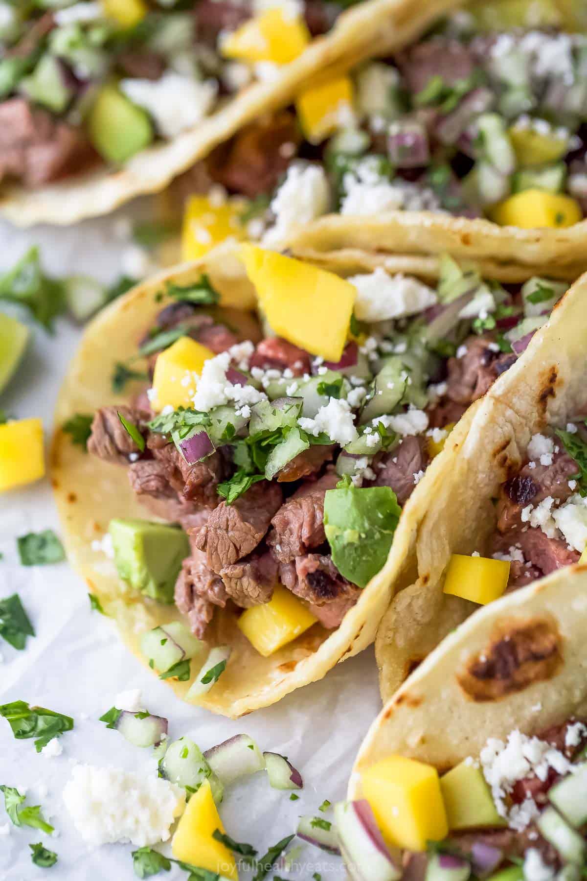 These 25-minute street tacos with tender steak are loaded with queso fresco, avocado, grilled onion, and lime juice for the perfect bite. Close-up of street tacos with toppings.