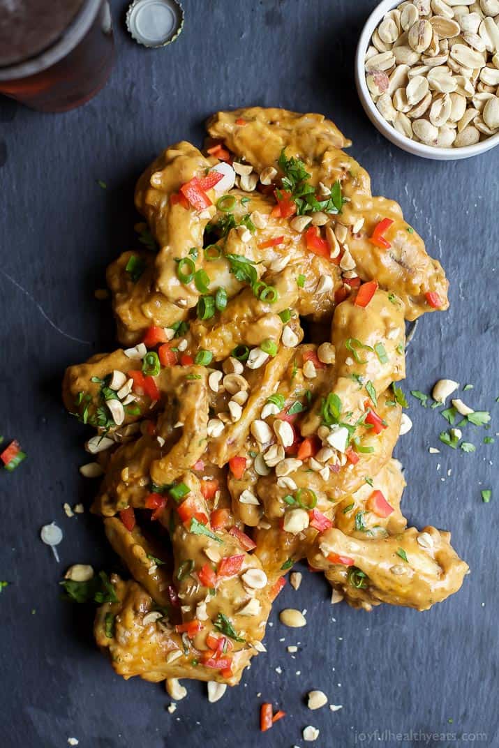 These Baked Chicken Wings with Spicy Peanut Sauce will have you licking your fingers clean! They're easy to make and healthier than ever. Baked chicken wings coated in Thai peanut sauce with a bowl of peanuts beside them