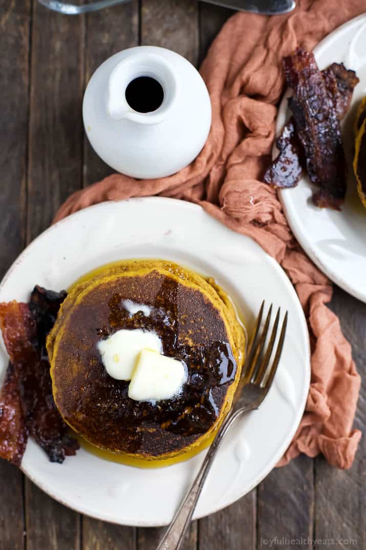 A plate of whole wheat pancakes beside a jar of pure maple syrup and a kitchen towel.
