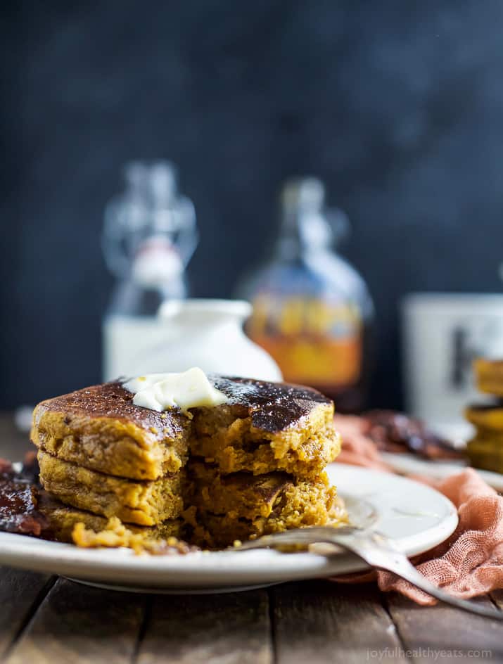 Three fluffy pumpkin pancakes stacked on a plate with a fork and some butter on top.