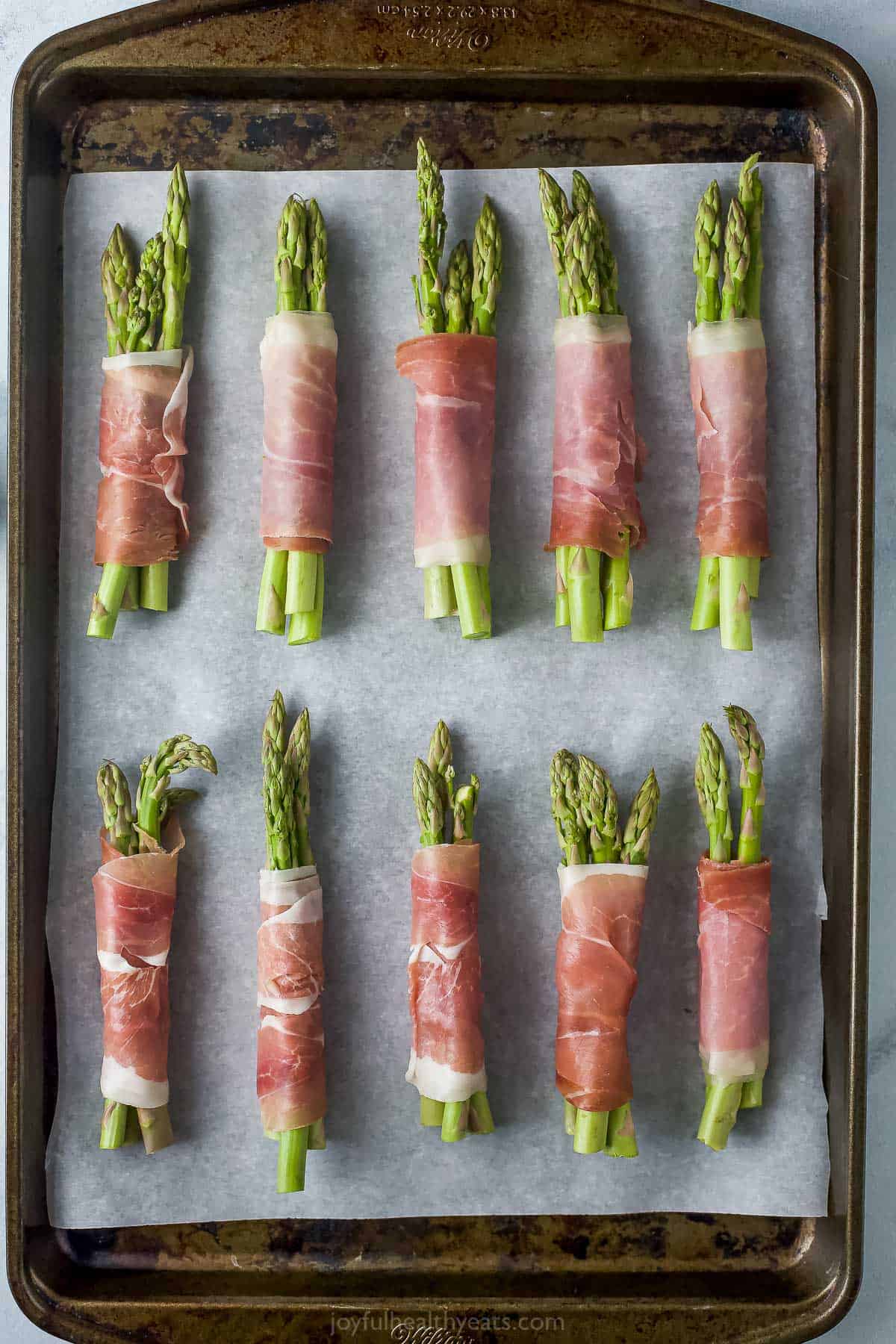 Ten unbaked asparagus wraps on a metal baking sheet lined with parchment paper