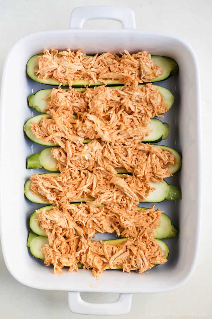 Top view of zucchini boats filled with shredded buffalo chicken in a baking dish