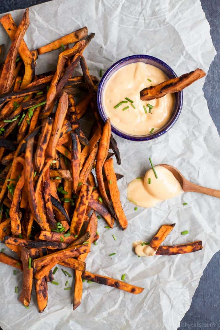 Served with a sweet and spicy honey sriracha sauce, these crispy baked sweet potato fries are an easy side dish that everyone will love! Crispy baked sweet potato fries on a sheet of parchment paper with a small bottle of honey sriracha sauce.