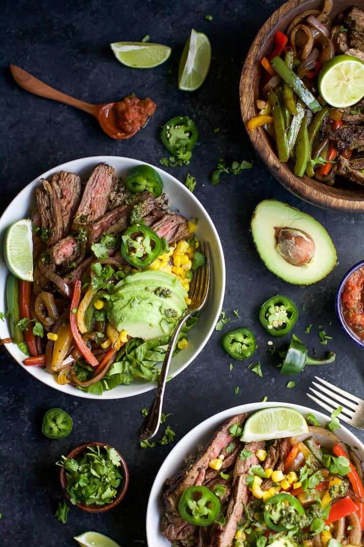 These 30-Minute Steak Fajita Burrito Bowls are filled with quinoa, fajita steak, creamy avocado, and a zesty cilantro-lime chimichurri sauce. a display of burrito bowls made with vegetables and sliced steak