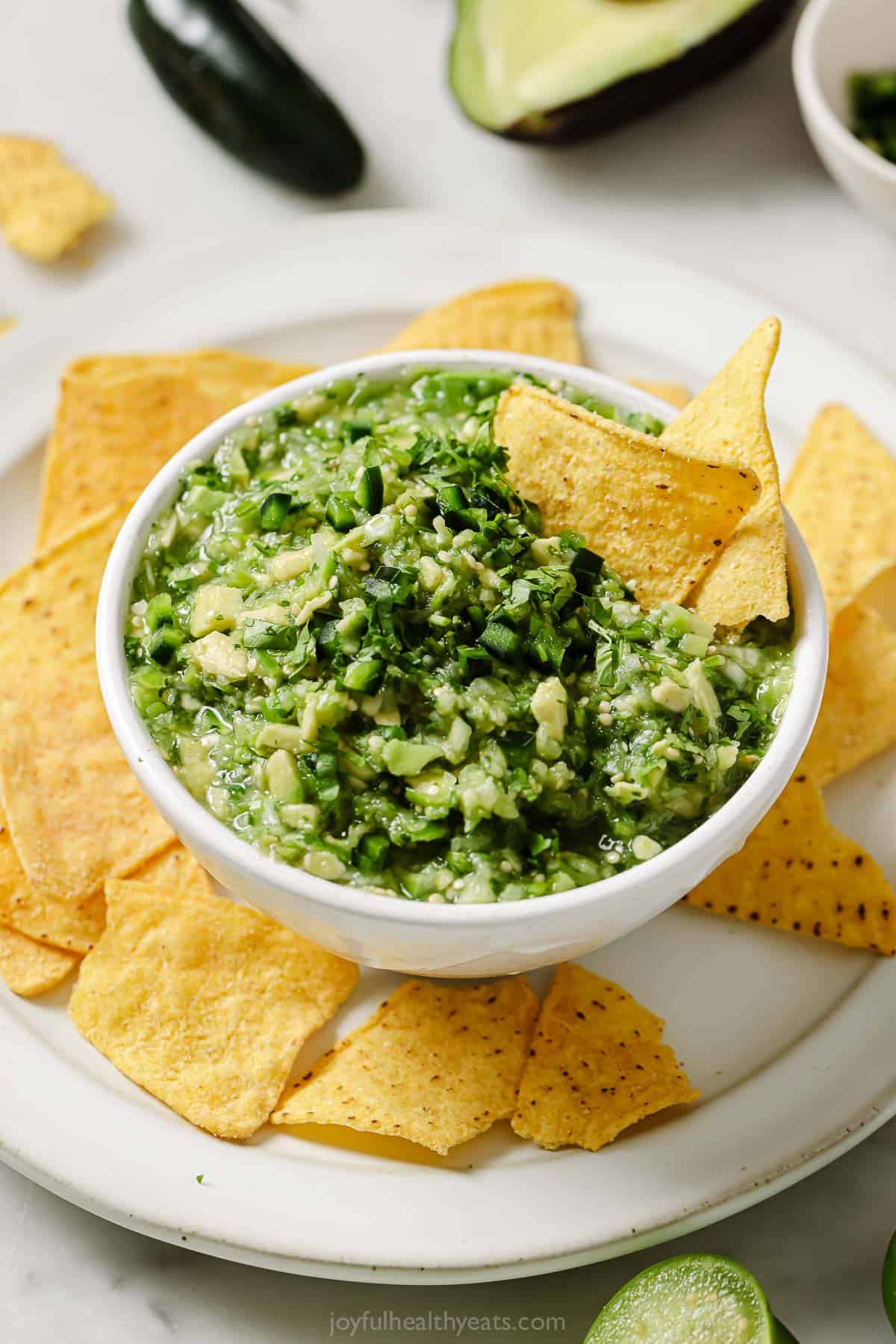 This spicy avocado salsa verde recipe with garlic, tangy lime juice, and fresh tomatillos is a 5-minute Mexican appetizer. A bowl of chunky avocado salsa verde with tortilla chips on the side.