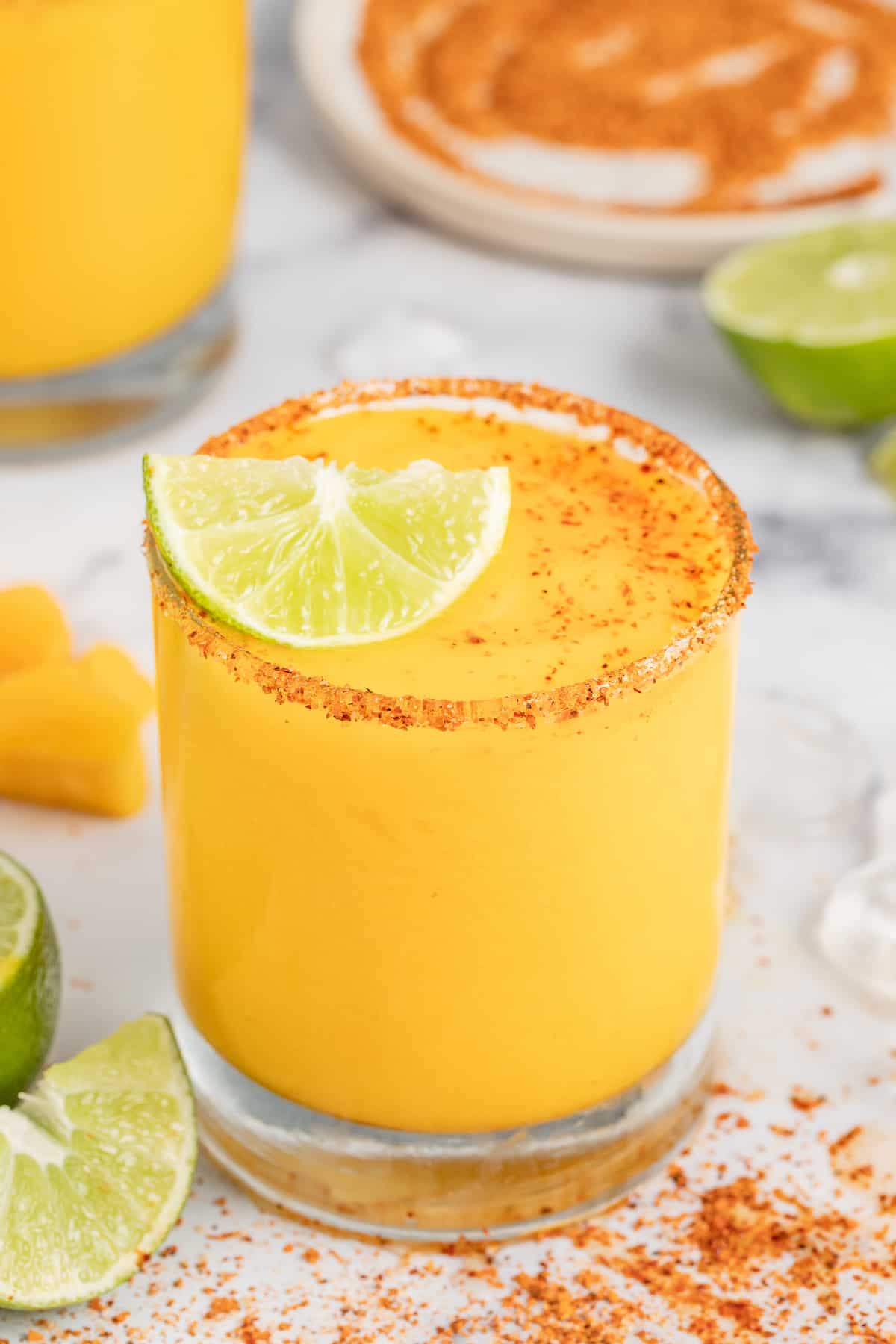 Served in chili-rimmed glasses, this frozen mango margarita is the boozy, tropical drink you need to beat the heat this summer. Frozen mango margarita with a lime wedge.
