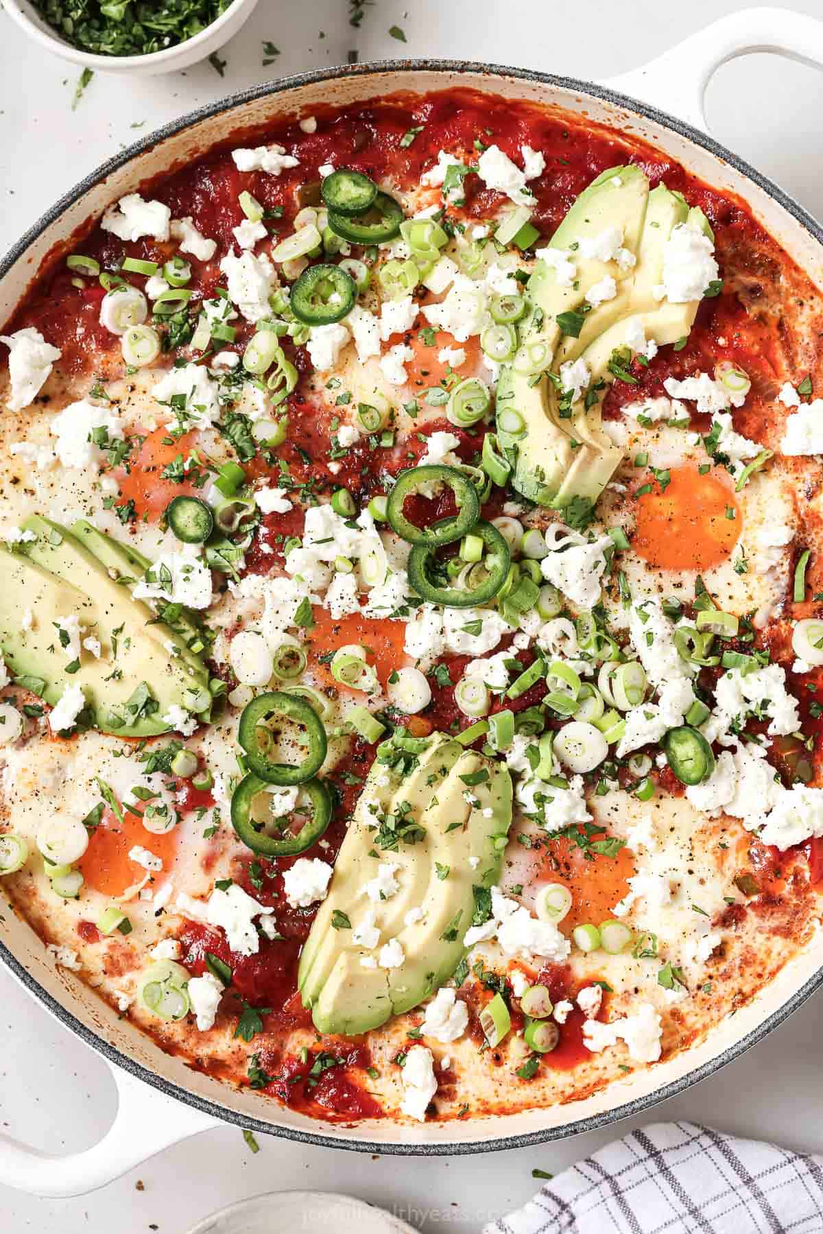 This saucy, one-skillet shakshuka recipe with poblanos, bell peppers, and onions in a smokey tomato sauce is perfect for brunch. Freshly-made one-skillet shakshuka with queso fresco, cilantro, green onions, jalapeños, and creamy avocado on top.