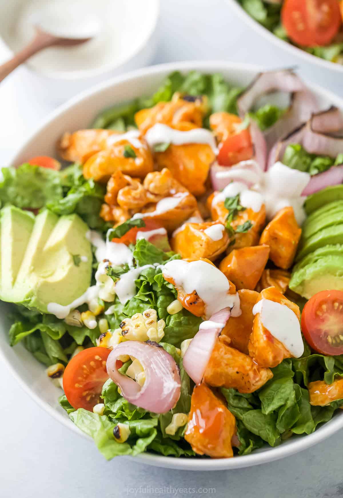This saucy buffalo chicken salad recipe with tomatoes, corn, and avocado is packed with fresh summer veggies for a light lunch. Buffalo chicken salad with Ranch dressing in a bowl.
