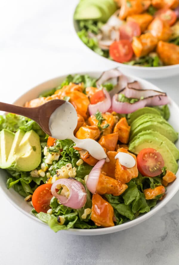 Spooning dressing over the chicken in the salad. 