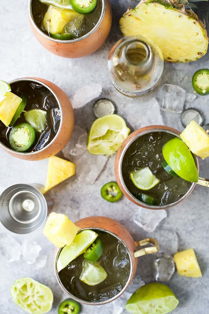 Top view of four Moscow Mules in copper cups surrounded by pineapple, limes, ice and jalapenos