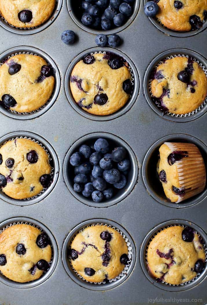 Studded with fresh berries and spiced with warm cinnamon, these whole wheat blueberry muffins are ready in 35 min. Perfect make-ahead snack! An overhead shot of a pan full of baked muffins with fresh berries scattered about