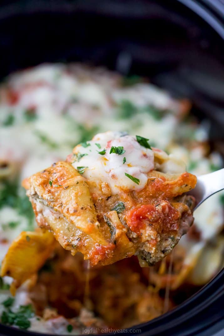 a spoon scooping stuffed shells from a crock pot