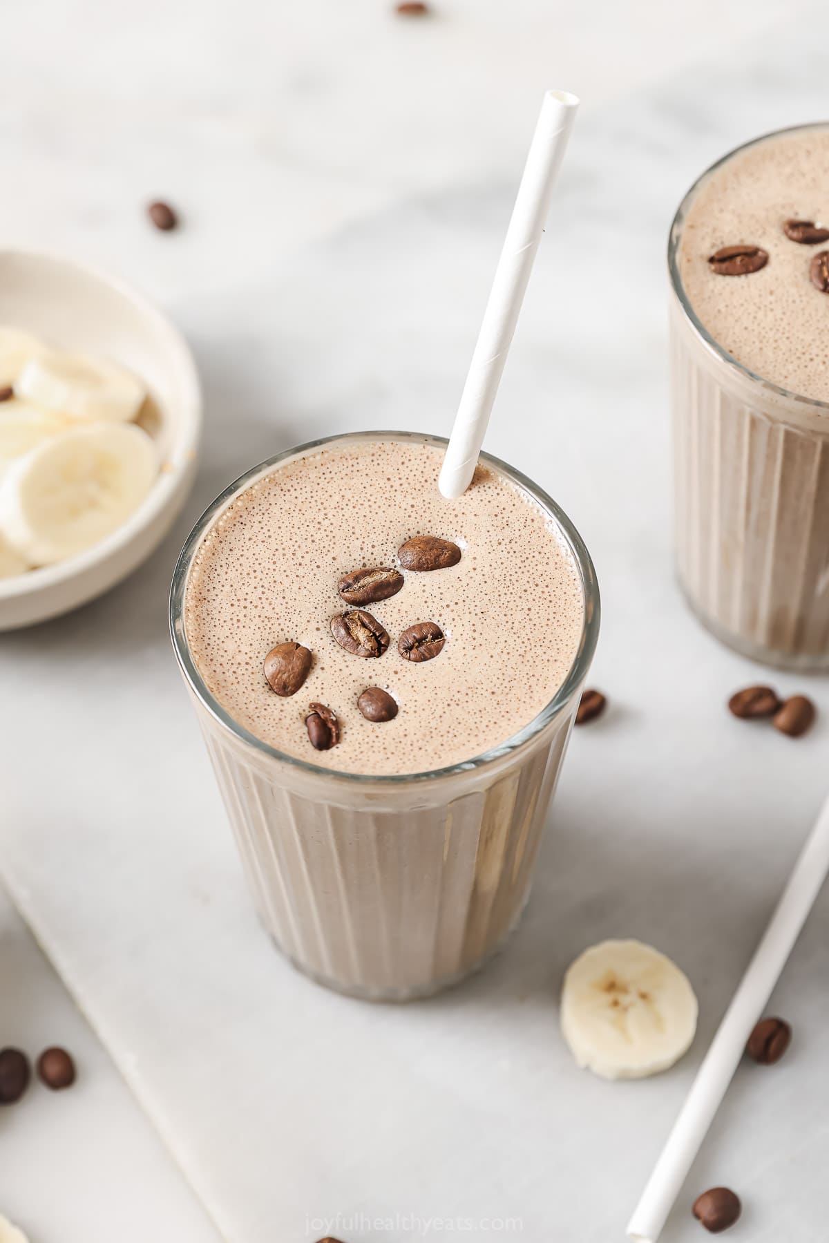 This creamy coffee smoothie recipe with vanilla protein powder and yogurt is a hearty way to kickstart your morning and stay awake all day. Creamy coffee smoothie in a tall glass with coffee beans on top.