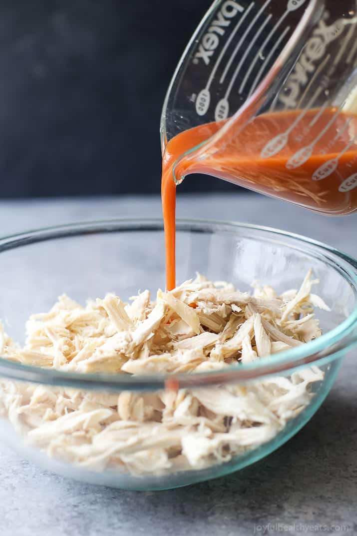 Hot sauce being poured over shredded chicken