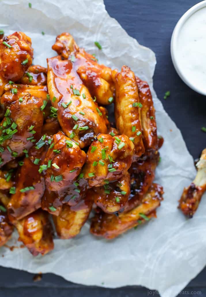 These crispy Baked BBQ Honey Wings are rubbed with a smoky spice blend and smothered in a homemade honey barbecue sauce infused with sriracha! Sweet and spicy chicken wings piled onto a piece of parchment paper with an empty bone beside them