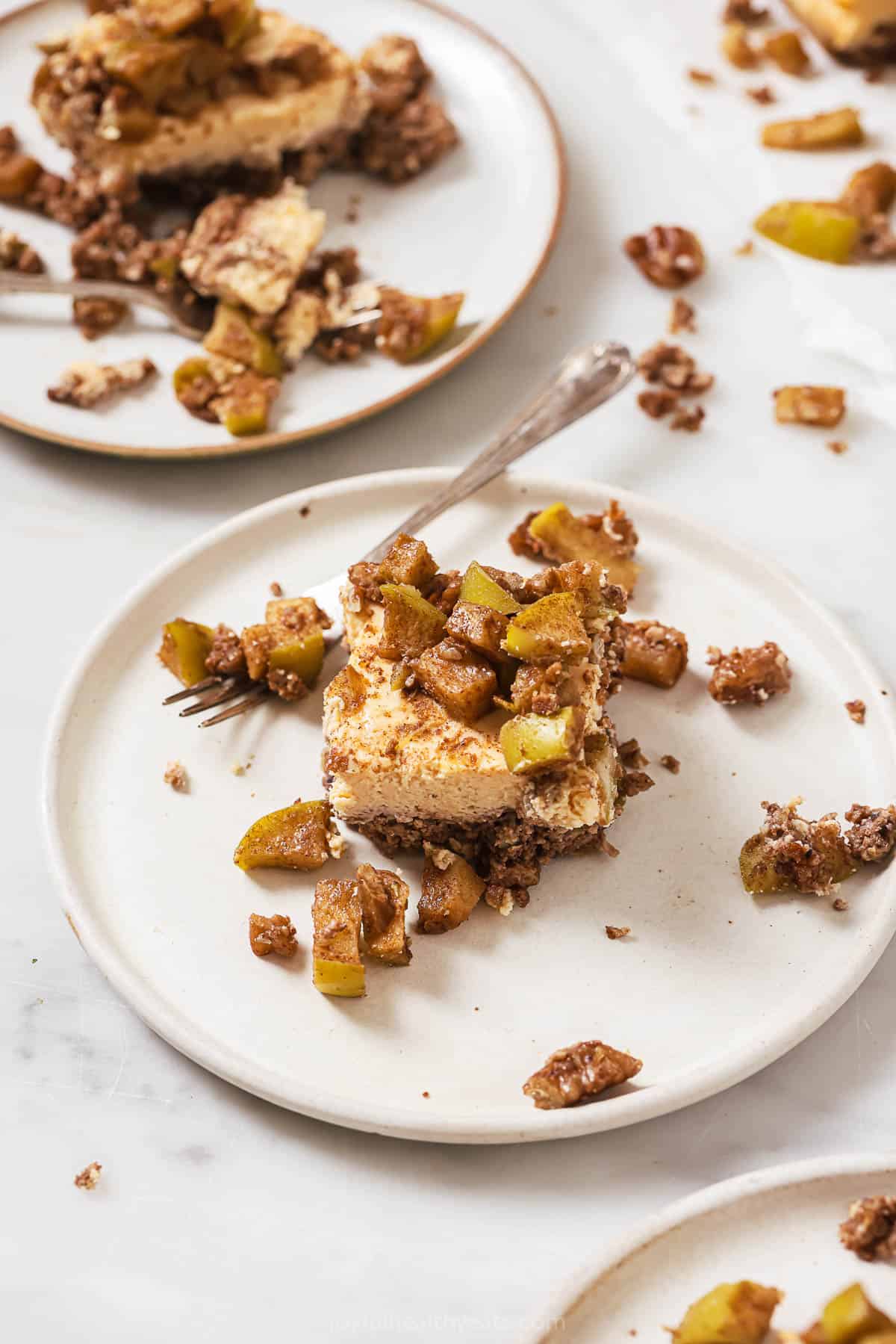 These creamy, baked apple cheesecake bars with a flourless pecan crust are the perfect fall treat with hints of cinnamon and maple syrup. One slice of apple cheesecake bars on a plate.
