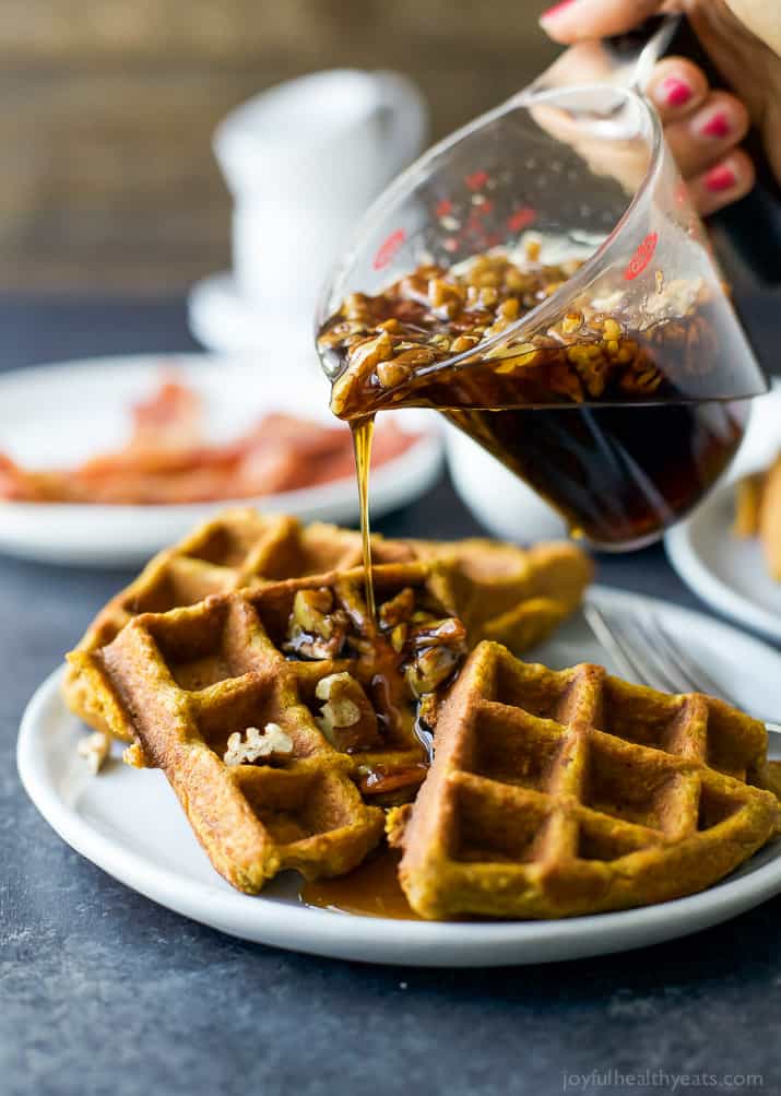 These gluten free pumpkin waffles are fluffy inside, crisp outside, with plenty of cozy spice. The best recipe to kickstart a fall morning! Vanilla pecan maple syrup being poured onto three quarters of a waffle