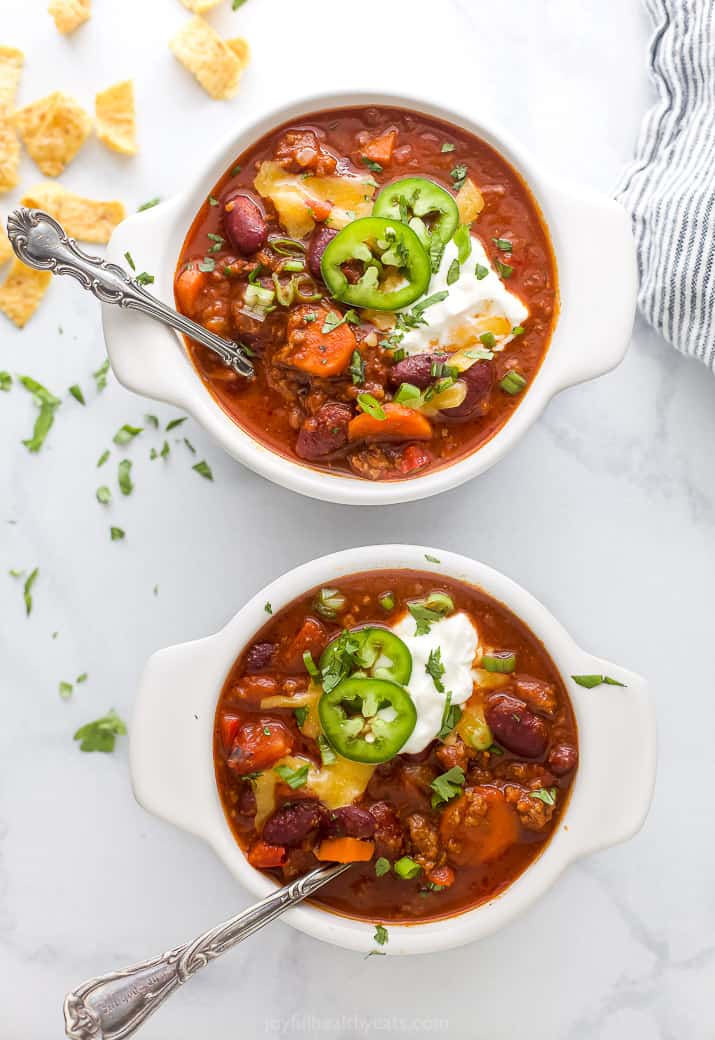 This easy beef chili recipe is packed full of flavor! Loaded with vegetables, ground beef, spices, and beans, it's the ultimate comfort food. Two bowls filled with beef chili and loaded with chili toppings.