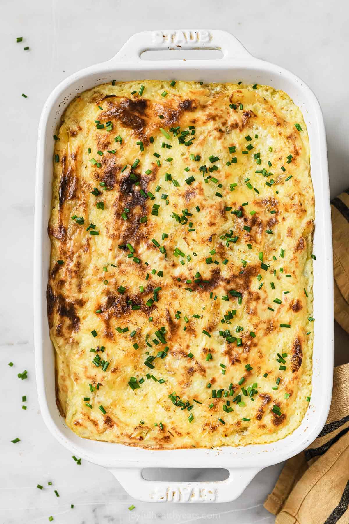 This thick and buttery sour cream and chive mashed potatoes recipe is the perfect side for all your holiday dinners. Sour cream and chive mashed potatoes in a baking dish.