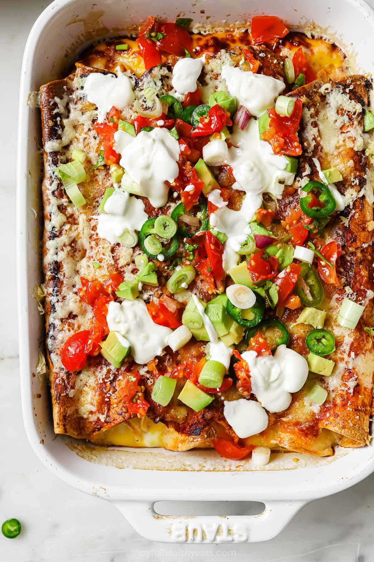 This breakfast enchiladas recipe has your favorite ingredients: bacon, ham, eggs, peppers, and spicy sauce for an easy overnight meal. Breakfast enchiladas with sour cream, avocado, and sliced jalapeños.