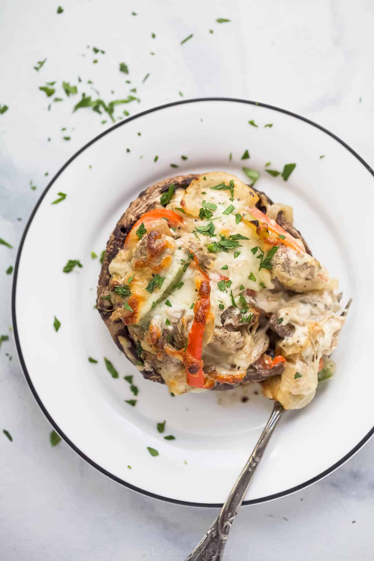 These Easy 30-Minute Philly Cheese Steak Stuffed Mushrooms are packed with tender steak, sautéed vegetables, and gooey cheese. stuffed mushroom on a plate with peppers and melted cheese