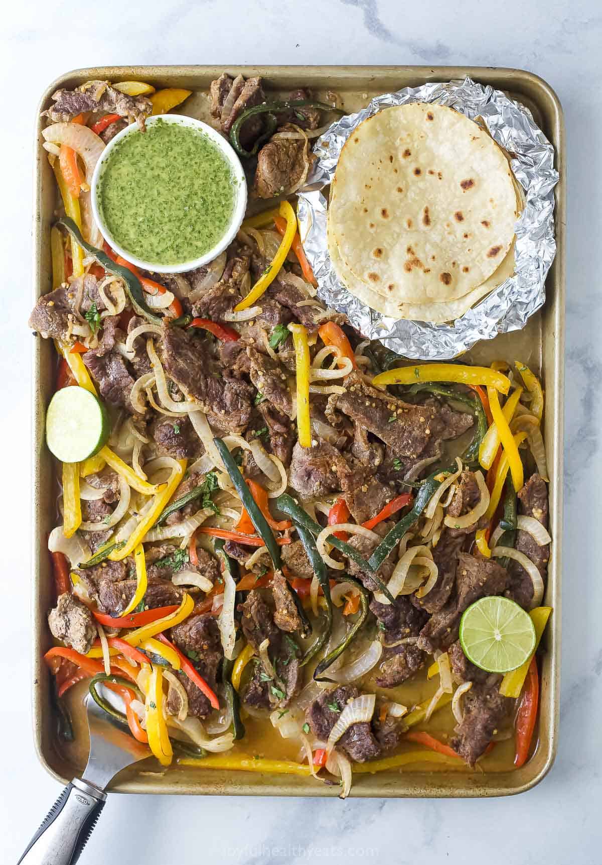 These sheet pan steak fajitas with bell peppers, sweet poblanos, and onions is a 30-minute dinner for weeknights and gatherings. They're perfect with a drizzle of homemade garlicky chimichurri. Sheet pan steak fajitas with cilantro chimichurri and flour tortillas on the side.