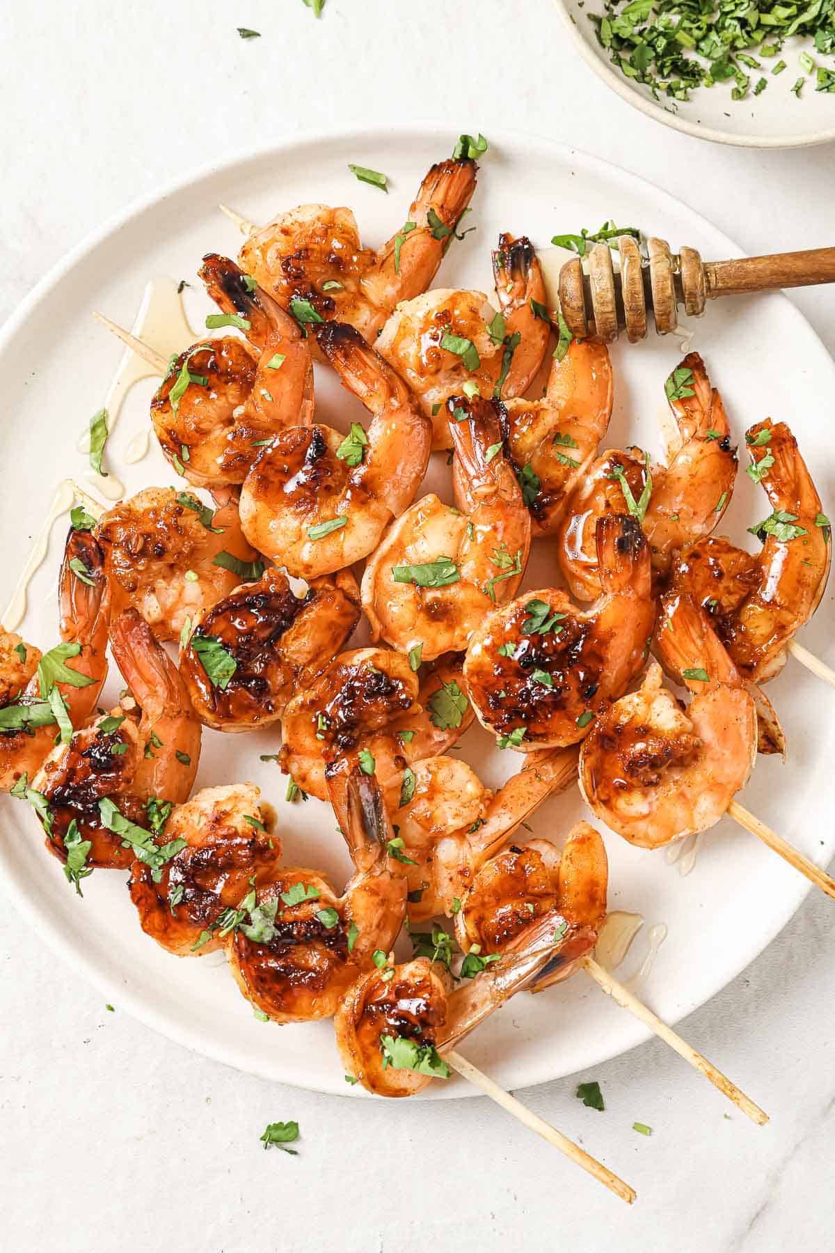 This freshly-grilled honey garlic shrimp recipe with spicy red pepper flakes is an easy 30-minute appetizer. Plate of honey garlic shrimp skewers with cilantro on top.