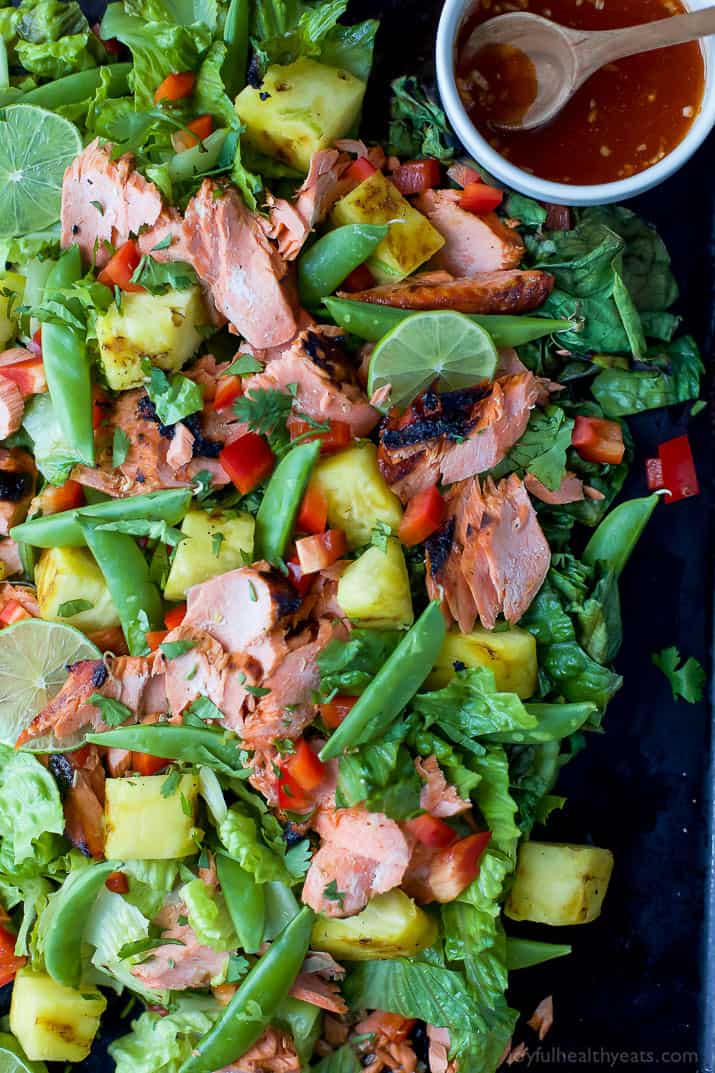 Sweet and spicy glazed salmon, crunchy charred lettuce, and juicy grilled pineapple combine with fresh veggies in this vibrant salmon salad! A platter full of salmon salad with some honey sriracha sauce in a small bowl on the side.