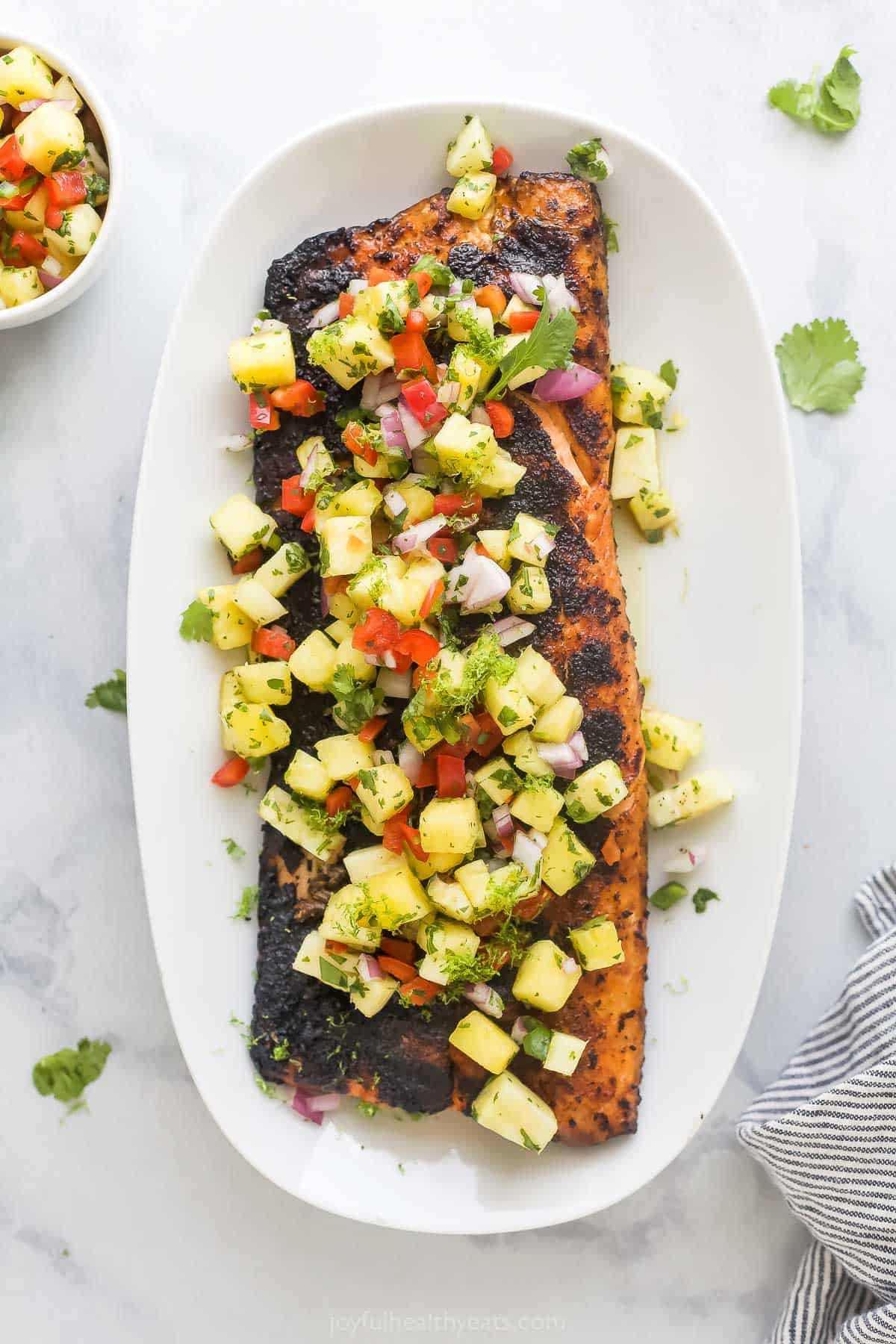 This chile-lime seasoned grilled salmon recipe with homemade spicy pineapple salsa is a 20-minute dinner for the summer. Whole grilled salmon with fresh pineapple salsa on a serving plate.