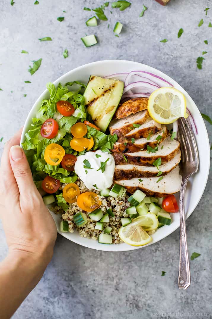 Loaded with fluffy quinoa and fresh vegetables, these easy Chicken Shawarma Bowls are a healthy weeknight dinner that everyone will adore. A hand grabbing a chicken shawarma bowl from a granite countertop