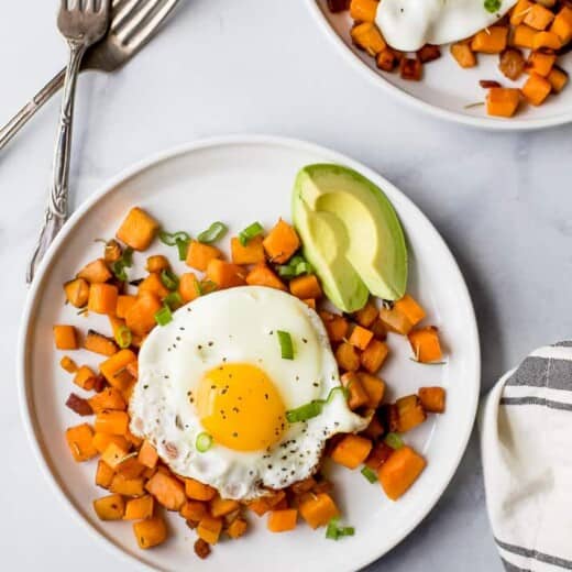 Breakfast hash with a sunny side-up egg and sliced avocado on the side.