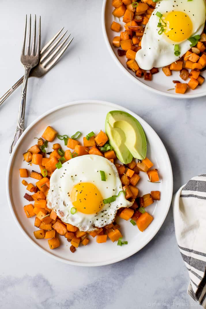 Breakfast hash with a sunny side-up egg and sliced avocado on the side. 