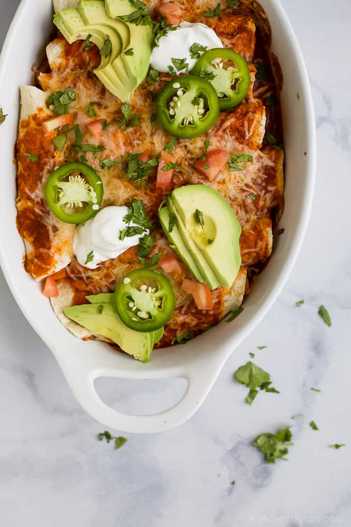 Angled photo of baked enchiladas with cilantro, chopped chili, and avocado.