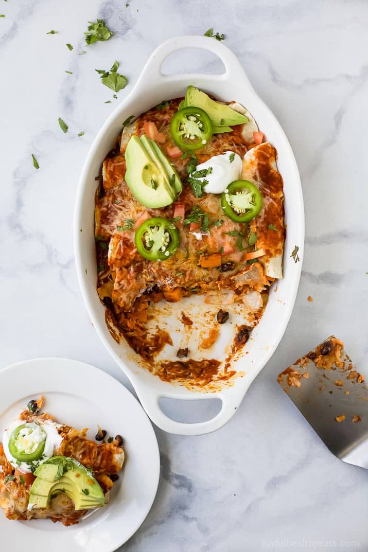 Sweet potato black bean enchiladas topped with cilantro, sliced avocado, and jalapeños in the baking dish. 