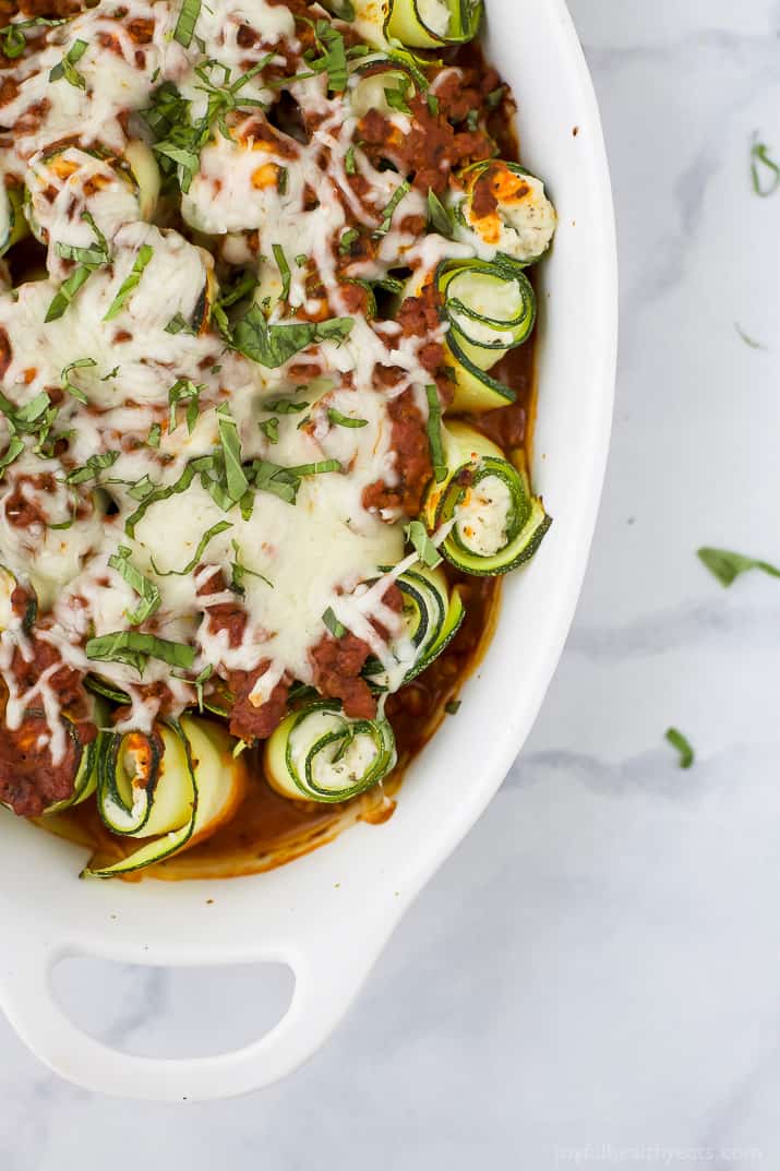 Angled photo of baked zucchini rolls with ricotta and tomato sauce. 