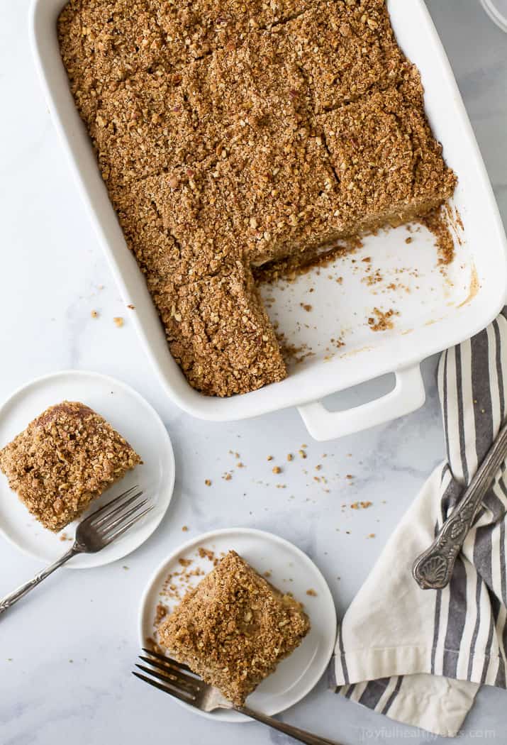 This apple coffee cake recipe with bold cinnamon flavor and crumbly nut topping is the perfect fall-flavored breakfast with your favorite coffee. Cinnamon-apple coffee cake in the baking pan, with two slices on serving plates to the side.