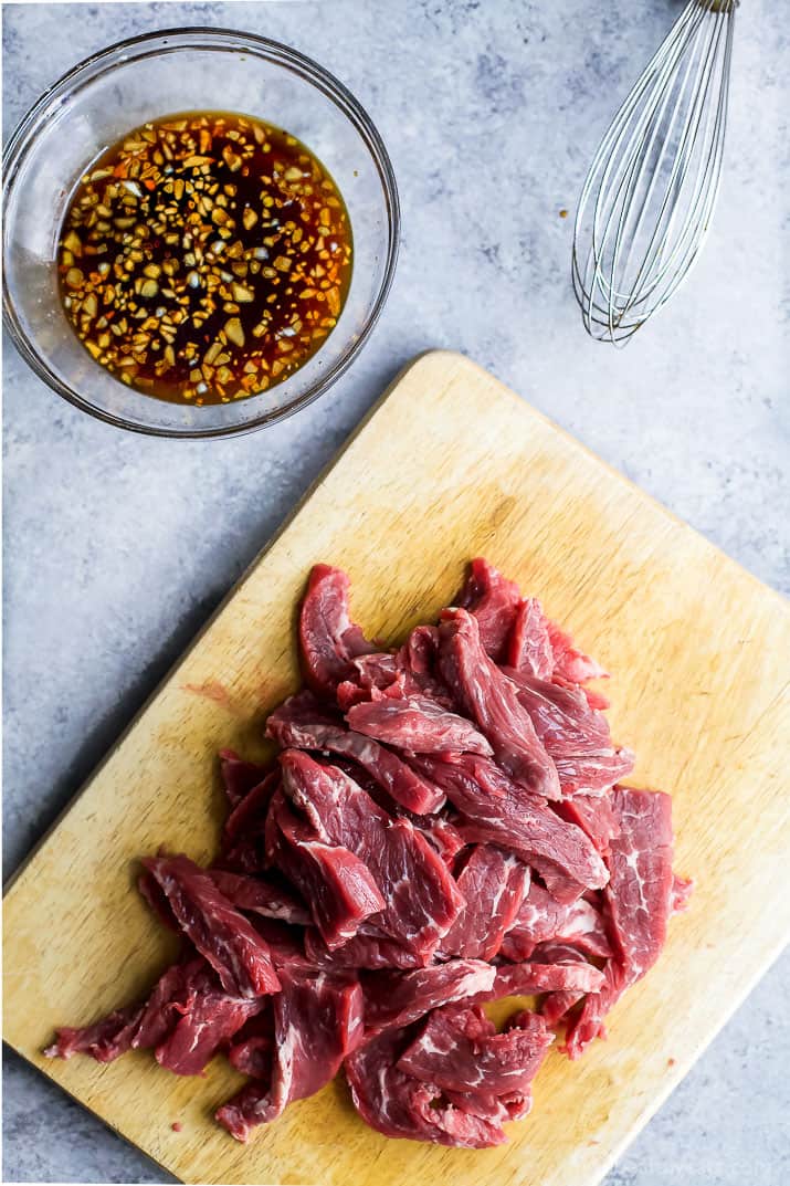 Overhead view of sliced beef on cutting board and bowl of sauce