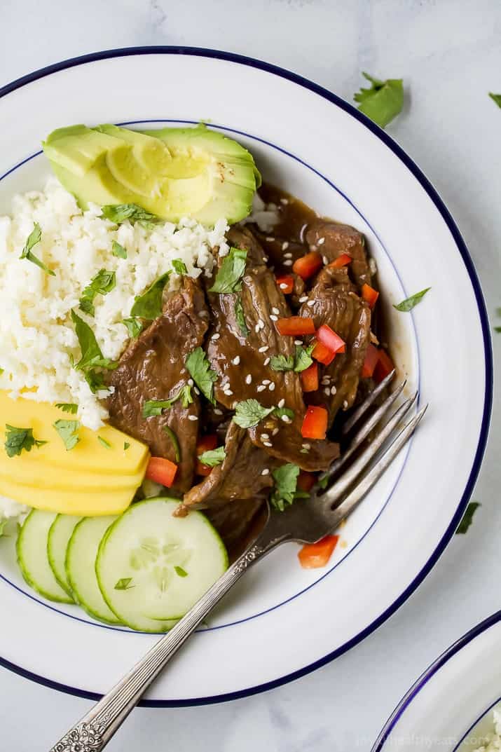 Instant Pot Korean Beef Bowls are a 30-minute meal that combines tender beef with a sweet, spicy sauce, cauliflower rice, veggies, and mango. Overhead view of Korean beef bowls with cauliflower rice and veggies