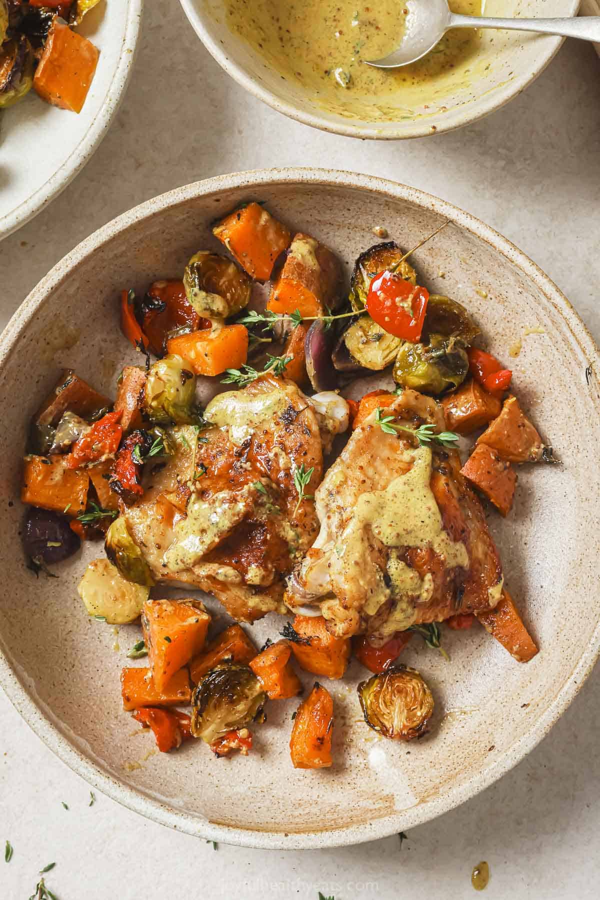 This sheet pan chicken thighs recipe with homemade honey-mustard sauce and roasted veggies is a hearty, little clean-up weeknight Sheet pan chicken thighs served with roasted veggies on a plate.